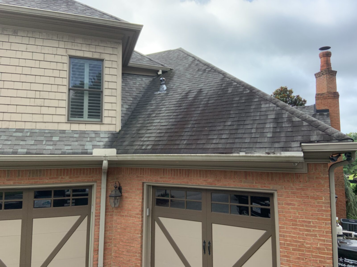 Residential house with two-car garage, brick exterior, and shingled roof. The roof shows streaks of discoloration. Consider professional roof cleaners for regular maintenance to keep it in top condition. Cloudy sky in the background adds a moody touch to the scene.