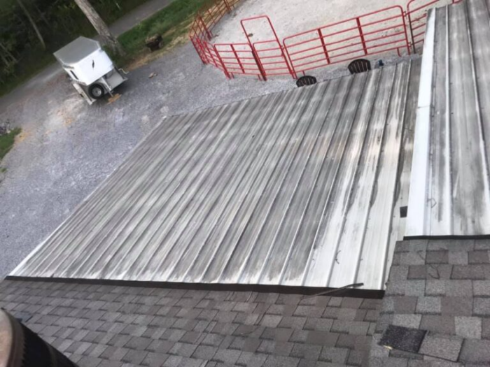 A metal roof panel has slid partially towards the ground from a shingled roof, with a gravel driveway and red fence visible in the background. This highlights the importance of professional roof maintenance in Knoxville to ensure your property's safety and maintain its curb appeal.