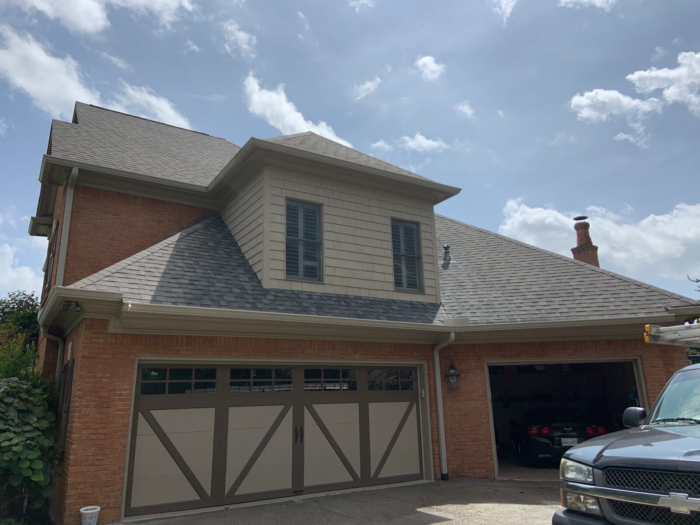 A two-story brick house with a double garage, one door open, under a partly cloudy sky. A blue truck is parked in the driveway, perhaps belonging to professional roof cleaners specializing in roof maintenance Knoxville.