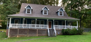 Nestled among lush greenery, this charming two-story blue house features a steep gabled roof with pristine white trim and an inviting front porch. Regular roof maintenance in Knoxville enhances its appeal, set beautifully against a backdrop of mature trees.