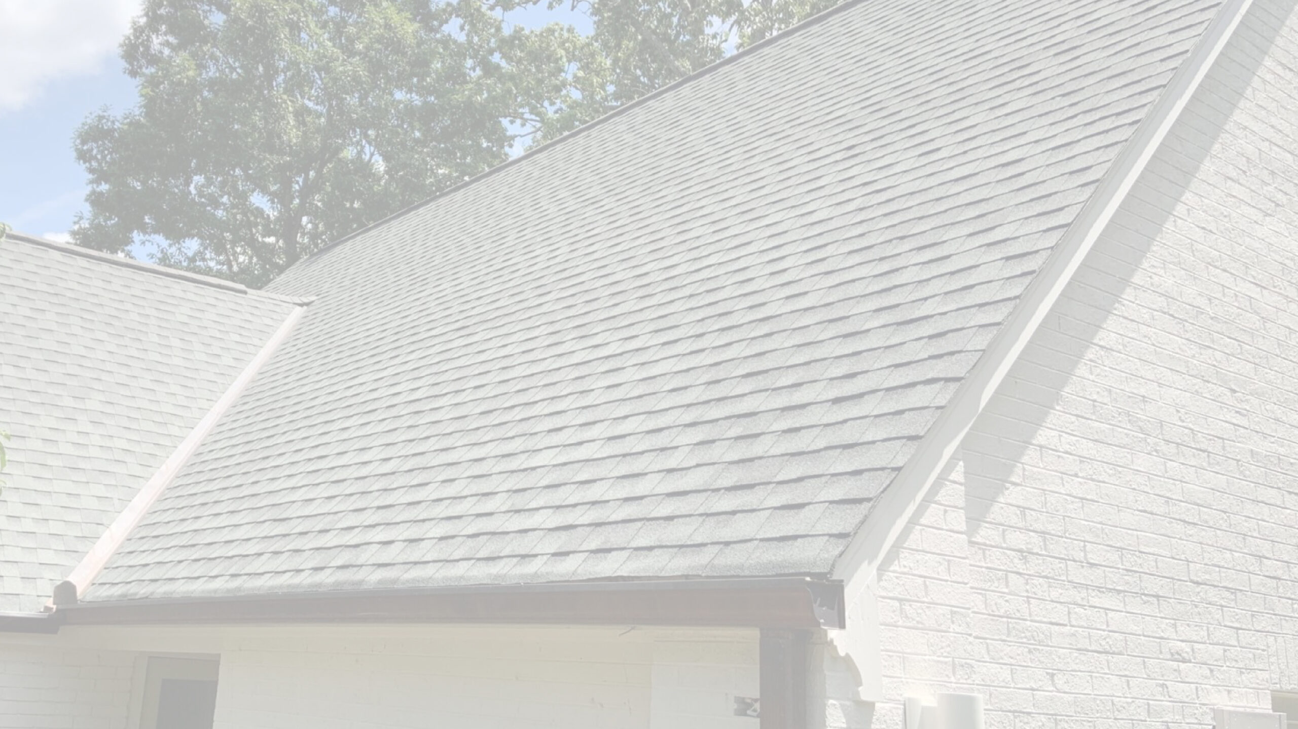 A steeply pitched roof with gray shingles on a house, partially shaded by nearby trees, highlights the importance of regular roof maintenance Knoxville residents prefer.